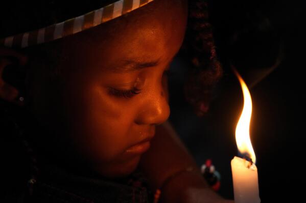A child holds a candle during a baptism ceremony inside the chapel of the Kalunga quilombo during the culmination of the week-long pilgrimage and celebration for the patron saint "Nossa Senhora da Abadia" or Our Lady of Abadia, in the rural area of Cavalcante in Goias state, Brazil, late Monday, Aug. 15, 2022. (AP Photo/Eraldo Peres)