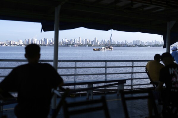 People look out at the coast of Belem, Brazil, as a boat nears shore, March 23, 2025. (AP Photo/Jorge Saenz, File)