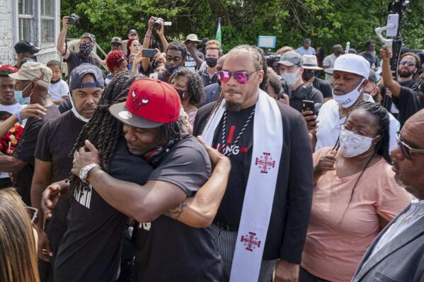 Local artist and business owner Ulysses Edwards, foreground wearing red Chicago Bulls cap, receives a hug from Khalil Ferebee, one of Andrew Brown Jr.'s sons, Sunday, May 2, 2021, in Elizabeth City, N.C., during a presentation of a mural honoring Brown that Edwards painted on an exterior wall of Brown's home on Perry Street. Public viewings were held Sunday for Brown in Hertford and then in Elizabeth City, where Brown was shot by Pasquotank County sheriff’s deputies serving warrants. (Chris Day/The Daily Advance via AP)
