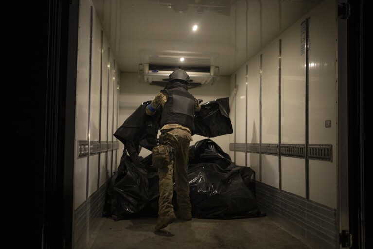 A member of Oleksii Yukov's body collector team piles the bodies of deceased Russians in a refrigerated truck in the Sloviansk region, Ukraine, Tuesday, Oct. 24, 2023. They retrieve bodies from the frontline to barter for Ukrainian bodies in periodic exchanges of war dead. (AP Photo/Bram Janssen)