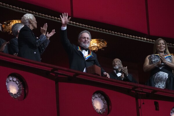 2023 Kennedy Center Honoree, comedian Billy Crystal, center, waves as he is applauded by fellow honorees Dionne Warwick and Queen Latifah, at the 46th Kennedy Center Honors at the John F. Kennedy Center for the Performing Arts in Washington, Sunday, Dec. 3, 2023. (AP Photo/Manuel Balce Ceneta)