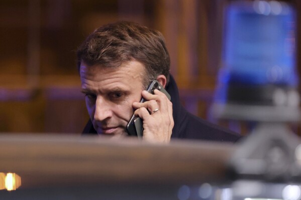 FILE -French President Emmanuel Macron speaks on a mobile phone as he departs from the European Union summit in Brussels on Thursday, Dec. 15, 2022.  French government officials on Monday accused Russia of waging a long-running online manipulation campaign against Ukraine's Western supporters.  By the second anniversary of Moscow's military invasion of its neighboring country.  (AP Photo/Olivier Mathis, File)