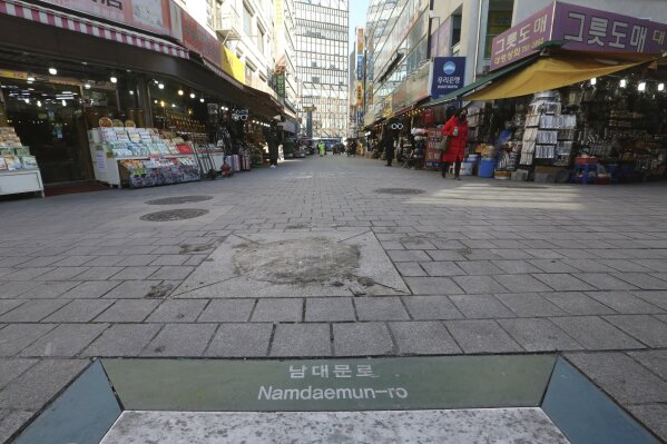 In this Tuesday, Feb. 18, 2020, photo, a woman wearing a face mask walks on the almost empty Namdaemun Market street in Seoul, South Korea. Even as cases and deaths from the new virus mount, fear is advancing like a tsunami - and not just in the areas surrounding the Chinese city of Wuhan, the center of the outbreak that has been declared a global health emergency. (AP Photo/Ahn Young-joon)