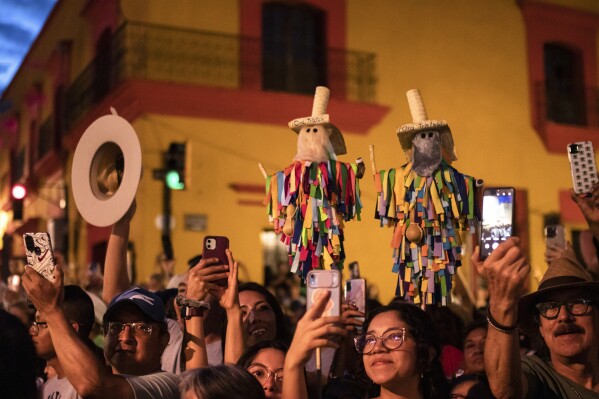 Spectators take photos of a parade during the Guelaguetza festival in Oaxaca, Mexico, Saturday, July 15, 2023. During the government-sponsored event, 16 Indigenous ethnic groups and the Afro-Mexican community promote their traditions through public dances, parades and craft sales. (AP Photo/Maria Alferez)