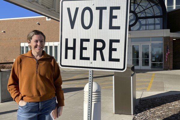 Molly Menton, 40, stands next to a "Vote Here" sign outside the Eden Prairie Library polling place in Eden Prairie, Minn., on Tuesday, March 5, 2024. Menton, who identifies as a lifelong Democrat in the Twin Cities suburb, said she voted for Joe Biden in the primary election. (AP Photo/Trisha Ahmed)
