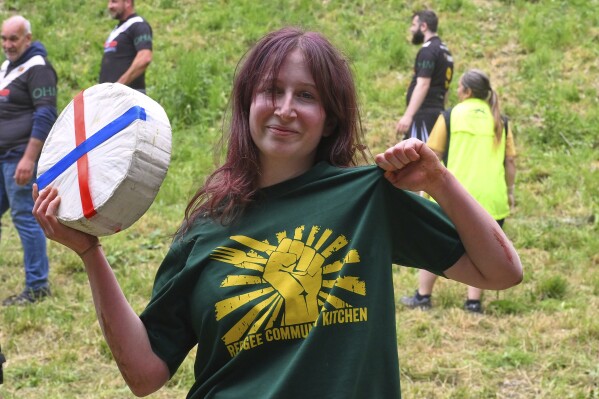 Ava Sender Logan shows the cheese roll after winning the women's downhill race category of the traditional annual Cheese Rolling contest at Cooper's Hill in Brockworth, Gloucestershire, England, Monday, May 26, 2025. (AP Photo/Anthony Upton)