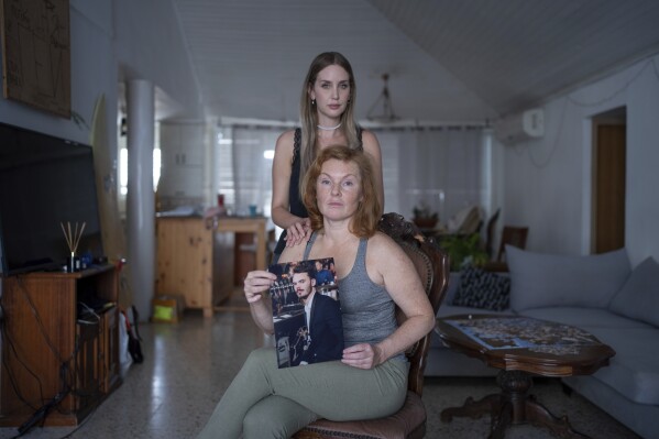 Evgenia Kozlov holds up a portrait of her 27-year-old son, Andrey Kozlov, while Kozlov's girlfriend Jenifer Master stands behind her in their family house in Rishon Lezion, Israel, Thursday, Oct. 26, 2023. Kozlov, a Russian citizen, was abducted by Hamas militants from the 