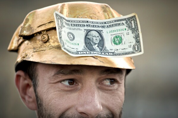 FILE - A man wears a one dollar bill on a miner's helmet painted in gold color in Bucharest, Romania, Sept. 21, 2013, during a protest against the exploitation of gold by by Gabriel Resources, a Canadian mining company, at Rosia Montana, the site of ancient Roman mining galleries in a mountainous western Romanian region and home to Europe's largest gold deposits. The Romanian government has won a years-long legal dispute with a Canadian mining company seeking financial damages over failed plans to open a gold and silver mine in the Eastern European country. (AP Photo/Vadim Ghirda, File)
