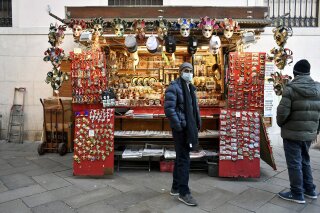 A vendor wearing a face mask stands by a stall in Venice, Italy, Friday, Feb. 28, 2020. Authorities in Italy decided to re-open schools and museums in some of the areas less hard-hit by the coronavirus outbreak in the country which has the most cases outside of Asia, as Italians on Friday yearned for a return to normal life even amid fears that the outbreak could plunge the country's economy into recession. (Claudio Furlan/Lapresse via AP)