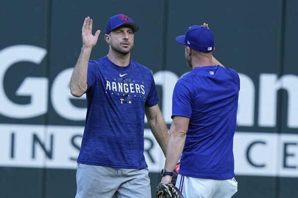 Texas Rangers starting pitcher Max Scherzer, left, gets a high five on the field during the team's baseball practice in Arlington, Texas, Tuesday, Oct. 17, 2023. The Rangers are scheduled to play the Houston Astros in Game 3 of MLB's American League Championship Series on Wednesday. (AP Photo/LM Otero)