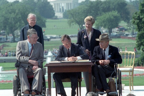 President George H. W. Bush signs the Americans with Disabilities Act during a ceremony on the South Lawn of the White House July 26, 1990. Joining the president are Rev. Harold Wilke, rear left, Evan Kemp, chairman of the Equal Opportunity Employment Commission, left, Sandra Parrino, chairman of the National Council on Disability; and Justin Dart, chairman of The President's Council on Disabilities. Jefferson Memorial is in background. (ĢӰԺ Photo/Barry Thumma)