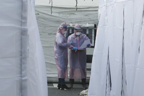 Medical staff wearing protective suits check documents as they wait for people with suspected symptoms of the new coronavirus, at a testing facility in Seoul, South Korea, Wednesday, March 4, 2020. The coronavirus epidemic shifted increasingly westward toward the Middle East, Europe and the United States on Tuesday, with governments taking emergency steps to ease shortages of masks and other supplies for front-line doctors and nurses. (AP Photo/Ahn Young-joon)