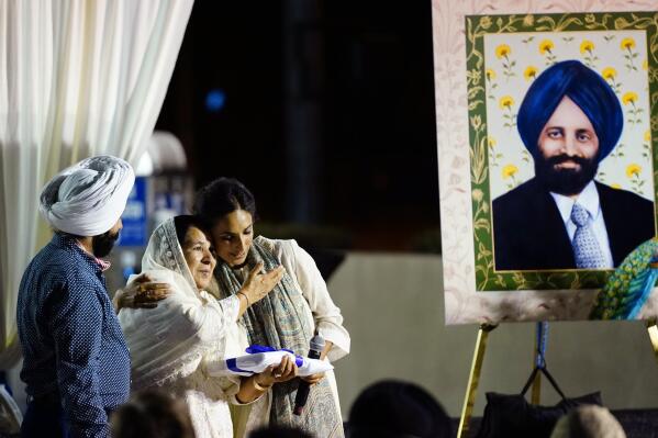 Valarie Kaur, right, of the Revolutionary Love Project, hugs Harjinder Kaur Sodhi, the widow of Balbir Singh Sodhi, middle, as Balbir's brother Rana Singh Sodhi, left, looks on at a memorial service on the 20th anniversary of the murder of Balbir Singh Sodhi Wednesday, Sept. 15, 2021, in Mesa, Ariz. Sikh businessman Balbir Singh Sodhi was helping plant a flower bed at his Arizona gas station when he was shot dead by a man seeking to avenge 9/11. Mistaken for an Arab Muslim because of his turban and beard, Sodhi was the first person to die in a wave of bias crimes unleashed by the attacks. (AP Photo/Ross D. Franklin)