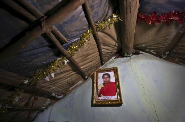 A portrait of Padmavathi, who died of COVID-19, hangs on the wall of her family hut made from bamboo and plastic sheeting  in a slum in Bengaluru, India, Thursday, May 20, 2021. Padmavathi collected hair, taking it from women's combs and hairbrushes to later be used for wigs. She earned about $50 a month. (AP Photo/Aijaz Rahi)