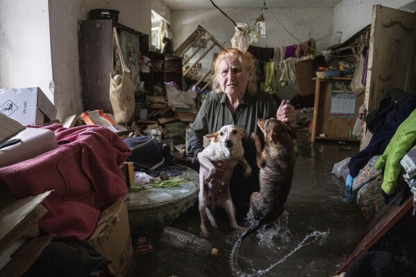 Tetiana holds her pet dogs, Tsatsa and Chunya, in her home that was flooded after the Kakhovka dam blew up overnight, in Kherson, Ukraine, on June 6, 2023. Ukraine accused Russian forces of blowing up the dam and hydroelectric power station, located in a part of southern Ukraine that Russia controls. (AP Photo/Evgeniy Maloletka)