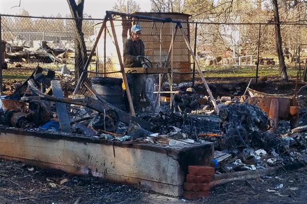 In this January 2019 photo provided by Sue Womack, James Holden sifts through the remains of his family's homestead, which burned to the ground in a 2018 wildfire, in Paradise, Calif. After fleeing one of the most destructive fires in California, the Holden family wanted to find a place that had not been so severely affected by climate change and chose Vermont. (Sue Womack via AP)