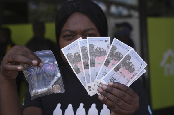 A woman holds the new Zimbabwean banknotes and coins called the ZiG, in the streets of Harare, Zimbabwe, Tuesday, April 30, 2024. Zimbabwe started circulating banknotes and coins for another new currency Tuesday in its latest attempt to solve a long-running and at times baffling monetary crisis that has seen the government try gold coins and a digital currency among other ideas. (AP Photo/Tsvangirayi Mukwazhi)
