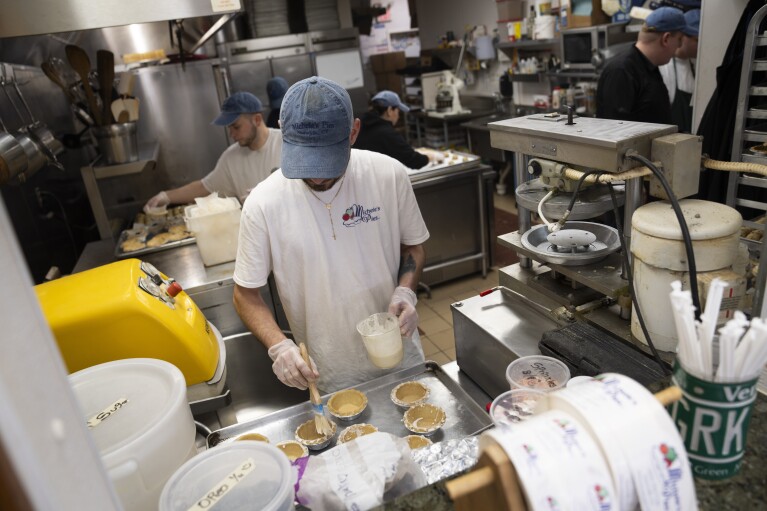 Employees work in a busy bakery kitchen at Michele's Pies, Wednesday, March 13, 2024, in Norwalk, Connecticut.  Math enthusiasts and bakers celebrate Pi Day on March 14 or 3/14, the first three digits of a mathematical constant with many practical uses.  Around the world, many people celebrate the day with a slice of sweet or savory pie.  (AP Photo/John Minchillo)