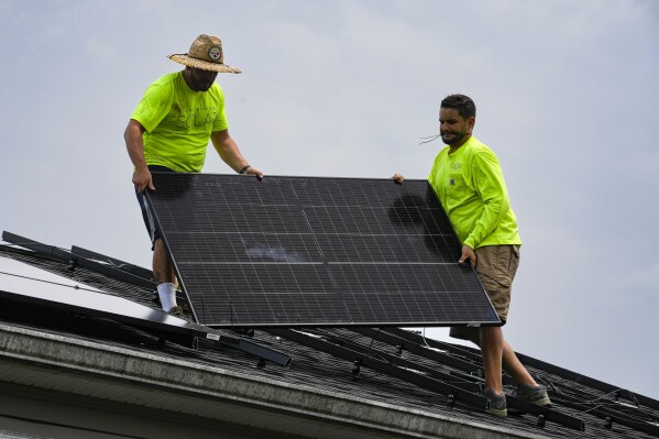 FILE - Even Berrios, left, and Nicholas Hartnett, owner of Pure Power Solar, install a solar panel on the roof of a home in Frankfort, Ky., July 17, 2023. The window to limit human-caused warming to a globally agreed goal is narrowing but still open because of the huge growth of solar energy and electric vehicles sales worldwide, a report said Tuesday, Sept. 26. (AP Photo/Michael Conroy, File)