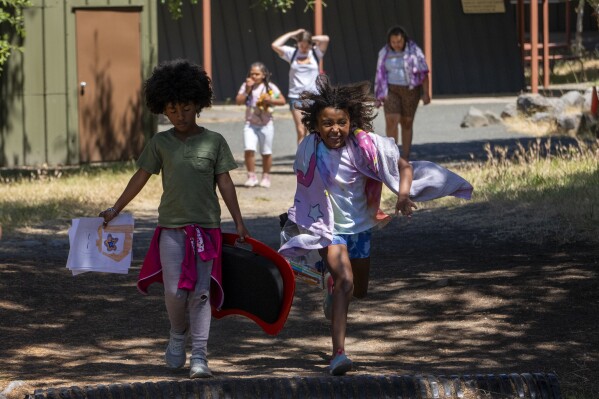 Charlotte Washington, 8, of East Lansing, Mich., right, and her new best friend, Alejandrina Chapman, 9, run together accompanied by their ever present art supplies during Camp Be’chol Lashon, a sleepaway camp for Jewish children of color, Thursday, July 27, 2023, in Petaluma, Calif., at Walker Creek Ranch. Unlike the other Jewish campers, Charlotte's parents found this camp after she told her father, who is an atheist, that she was interested in converting to Judaism. She now attends a synagogue and will take Bat Mitzvah classes. (AP Photo/Jacquelyn Martin)