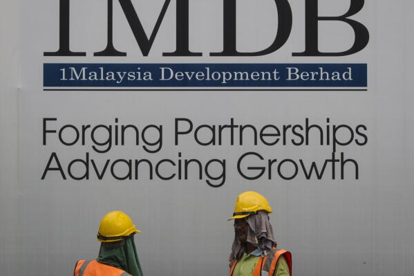 FILE - In this May 14, 2015, file photo, construction workers chat in front of a billboard for state investment fund 1 Malaysia Development Berhad (1MDB) at the fund's flagship Tun Razak Exchange development in Kuala Lumpur, Malaysia. Malaysia's Finance Ministry said Monday, May 10, 2021 that sovereign wealth fund 1MDB and a former subsidiary have filed 22 lawsuits to recover assets worth over $23 billion from various institutions and individuals. (AP Photo/Joshua Paul, File)