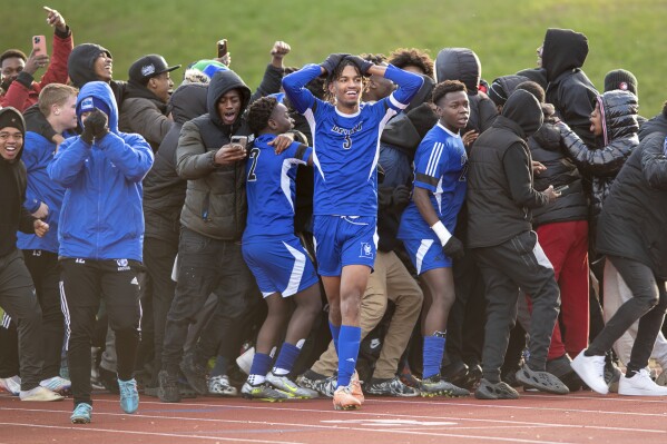 Caden Boone, center, celebrates with teammates and fans after defeating Deering 3-2 in overtime high school soccer to capture the Class A State Boys Soccer Championship, Saturday, Nov. 12, 2023 in Oakland, Maine. The boy's team in the Maine city that was the site of a mass shooting more than two weeks ago won the state title. (Russ Dillingham/Sun Journal via AP)