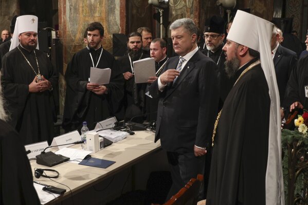 
              Ukrainian President Petro Poroshenko, second right, crosses himself with the new head of Ukrainian Orthodox church Metropolitan Epiphanius, right, during a closed-door synod of three Ukrainian Orthodox churches to approve the charter for a unified church and to elect leadership in the St. Sophia Cathedral in Kiev, Ukraine, Saturday, Dec. 15, 2018. Ukrainian Orthodox leaders say they have approved the creation of a unified church independent of the Moscow Patriarchate and elected a leader to head the new church. The leader of the new autocephalous Ukrainian Orthodox Church will be Metropolitan Epiphanius, a 39-year-old bishop from the Kiev Patriarchate. (Mikhail Palinchak, Ukrainian Presidential Press Service/Pool Photo via AP)
            