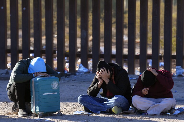 Migrants rest in the desert near the border wall as they join hundreds of migrants gathered at the border in Lukeville, Ariz., Tuesday, Dec. 5, 2023.  (AP Photo/Ross D. Franklin)