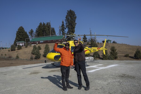 Majeed Bakshi, left, owner of heliskiing company and pilot captain Deeraj wave at a helipad in Gulmarg, northwest of Srinagar, Indian controlled Kashmir, Saturday, Jan. 13, 2024. Bakshi said that these helicopters were used for heliskiing, but due to a lack of snow, they decided to offer joy rides to tourists to compensate for losses. (AP Photo/Dar Yasin)