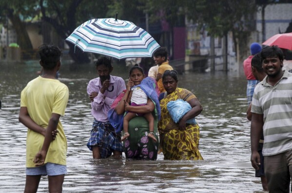 FILE - People wade through a flooded street in Chennai, India, Nov. 25, 2020. Voters in India, from the rain-drenched Himalayas in the north to the sweltering, dry south, are looking for politicians who promise relief, stability and resilience to the wide-ranging and damaging effects of a warming climate. (AP Photo/R. Parthibhan, File)