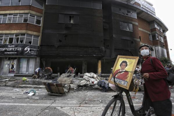 A woman walks past La Luna hotel that was burned and looted Monday night during a protest against tax reform in Cali, Colombia, Tuesday, May 4, 2021. Colombia's finance minister resigned on Monday following five days of protests over a tax reform proposal that left at least 17 dead. (AP Photo/Andres Gonzalez)
