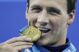 FILE - Ryan Lochte, of the United States, bites his gold medal for the men's 200 meters freestyle at the FINA Swimming World Championships in Shanghai, China, on July 26, 2011. Ryan Lochte told The Associated Press by phone Sunday, July 3, 2022, that he is auctioning off all of his Olympic silver and bronze medals, with the proceeds going to a charity benefitting children. The 37-year-old swimmer earned 12 medals over four Olympics, including six gold that he plans to keep for now. (AP Photo/Michael Sohn, File)