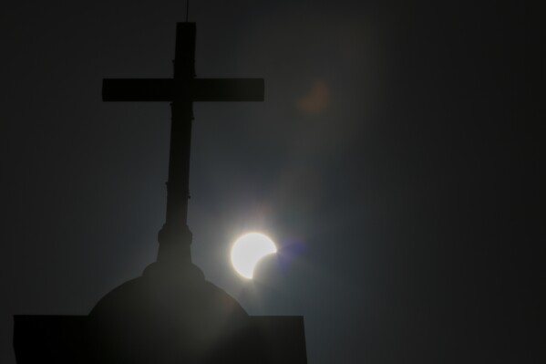 FILE - A partial solar eclipse is seen behind a cross on the steeple of the St. George church, in downtown Beirut, Lebanon, Sunday, June 21, 2020. Throughout history, solar eclipses have had profound impact on adherents of various religions around the world. They were viewed as messages from God or spiritual forces, inducing emotions ranging from dread to wonder. (AP Photo/Hassan Ammar, File)
