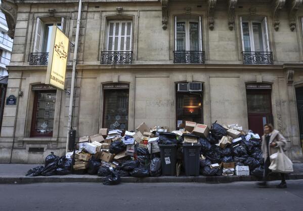 A woman walks past an uncollected garbage pile in Paris, Monday, March 20, 2023. France's government is fighting for its survival Monday against no-confidence motions filed by lawmakers who are furious that President Emmanuel Macron used special constitutional powers to force through an unpopular bill raising the retirement age from 62 to 64 without giving them a vote. (AP Photo/Aurelien Morissard)