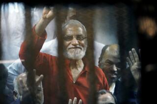 FILE - In this May 16, 2015 file photo, Muslim Brotherhood spiritual leader, Mohammed Badie waves from a defendants cage in a makeshift courtroom at the national police academy, in eastern Cairo, Egypt. On Sunday, July 11, 2021, Egypt's highest appeals court upheld the sentencing of ten leaders of Egypt’s outlawed Muslim Brotherhood, including Badie, to life imprisonment, the state-owned MENA news agency reported. In 2019, a Cairo criminal court found all ten guilty of charges related to killing policemen and organizing mass jail breaks during Egypt's 2011 uprising. (AP Photo/Ahmed Omar, File)