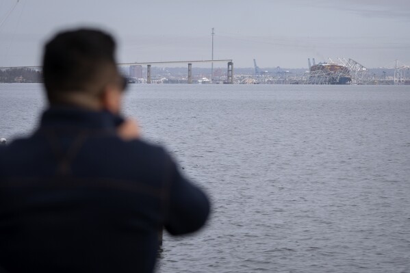 A bystander looks at the wreckage of the Francis Scott Key Bridge on Tuesday, March 26, 2024, as seen from Pasadena, Md. (AP Photo/Mark Schiefelbein)