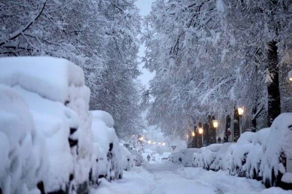 A man walks through snow covered roads after heavy snow fall in Munich, Germany, Saturday, Dec. 2, 2023. (AP Photo/Matthias Schrader)