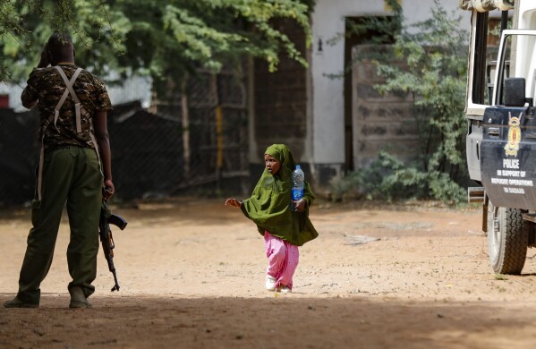 A Somali refugee girl walks past an armed Kenyan policemen outside a field hospital of the International Rescue Committee (IRC) at the Dadaab refugee camp in northern Kenya Friday, July 14, 2023. One of the world's largest refugee camps offers a stark example of the global food security crisis with thousands of people fleeing Somalia in recent months to escape drought and extremism but finding little to eat when they arrive at the Dadaab camp in neighboring Kenya. (AP Photo/Brian Inganga)