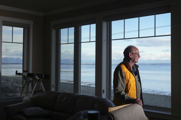 Real estate agent Hugh Wilson, who says Airbnb listings he manages have faced a higher cancellation rate than usual, stands for a portrait at an Airbnb overlooking Boundary Bay and British Columbia in the distance on Maple Beach, Monday, March 17, 2025, in Point Roberts, Wash. (AP Photo/Lindsey Wasson)