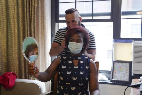 Elizabeth Deterville looks at her new hairstyle courtesy of stylist Roberto Novo in an apartment Wednesday, May 5, 2021 in New York. Novo started offering older clients free haircuts during the coronavirus pandemic. (AP Photo/Emily Leshner)