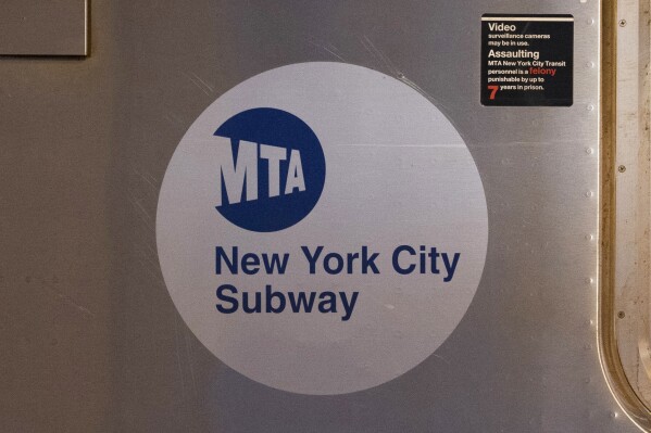FILE - The MTA logo is seen on the side of a New York City subway car, April 23, 2020, in the Queens borough of New York. A man set a cup of liquid on fire and tossed it at fellow subway rider in New York City, setting the victim's shirt ablaze and injuring him. The random attack happened on a No. 1 train in lower Manhattan on Saturday afternoon, May 25, 2024, city police said, adding that the suspect was in custody. (AP Photo/Mark Lennihan, File)