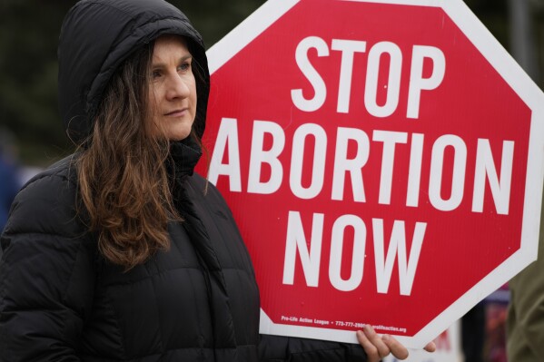 FILE - Kinga Gebauer holds a sign in front of the Walgreens corporate headquarters during a protest over plan to sell abortion pills Walgreens Deerfield Headquarters in Deerfield, Ill., Tuesday, Feb. 14, 2023. An Associated Press-NORC Center poll found that most U.S. adults favor allowing abortion at least in the early weeks of pregnancy. (AP Photo/Nam Y. Huh, File)