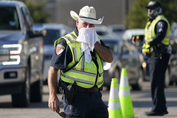 FILE - Police officer James Rhodes uses a wet towel to cool off as he directs traffic after a sporting event in Arlington, Texas, Saturday, Aug. 19, 2023. Another record-setting day of high temperatures is forecast in the Dallas/Fort Worth area Saturday, Aug. 26, 2023, before a slight cooling trend moves into the area, according to the National Weather Service as heat warnings stretch from the Gulf Coast to the Southeastern U.S. and upper Mid-South. (AP Photo/LM Otero, File)