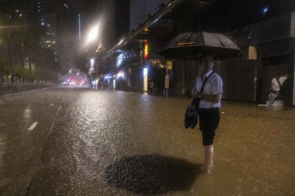 A pedestrian waits for a bus on a flooded street following heavy rainstorms in Hong Kong, Friday, Sept. 8, 2023. (AP Photo/Louise Delmotte)