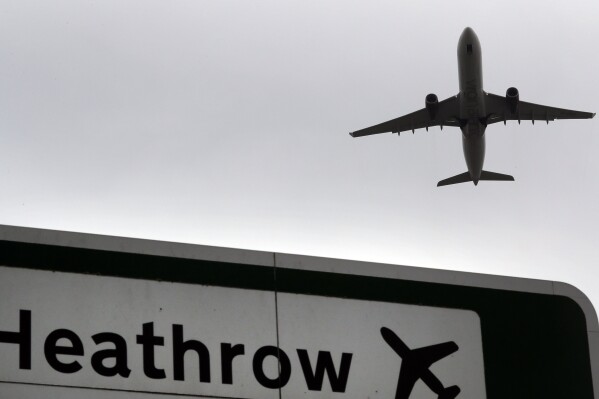 FILE - A plane takes off over a road sign near Heathrow Airport in London, June 5, 2018. The British government says it will grant extensions to several large U.K. airports unable to meet the June 1, 2024 deadline to fully install new scanning technology that would have allowed passengers to take two liters (70 ounces) of liquid in their hand luggage — rather than the current paltry 100 milliliters (3.5 ounces). (AP Photo/Kirsty Wigglesworth, file)
