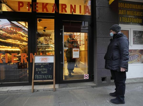 FILE - A customer inside a bakery wearing a face mask walks to the door, in Warsaw, Poland, Nov. 26, 2021. Poland is abolishing practically all of its COVID-19 restrictions next week, a government official said Thursday March 24, 2022. People will no longer be required to wear masks in indoor public spaces starting Monday March 28, Health Minister Adam Niedzielski said. The only exception will be in medical facilities, where staff and patients will still need to wear them. (AP Photo/Czarek Sokolowski, File)