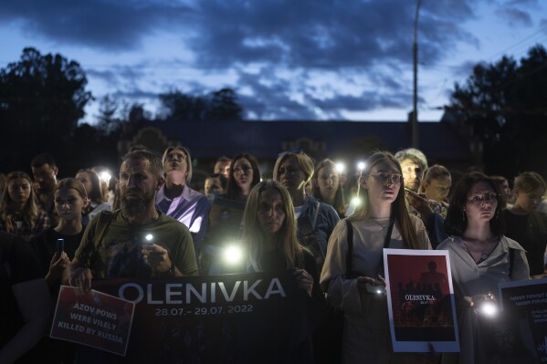 People hold signs as they gather outside the Russian Embassy in Kyiv, Ukraine, Saturday, July 29, 2023, to mark one-year anniversary of the attack on a prison building in Olenivka, eastern Ukraine, that killed dozens of Ukrainian military prisoners. (AP Photo/Jae C. Hong)