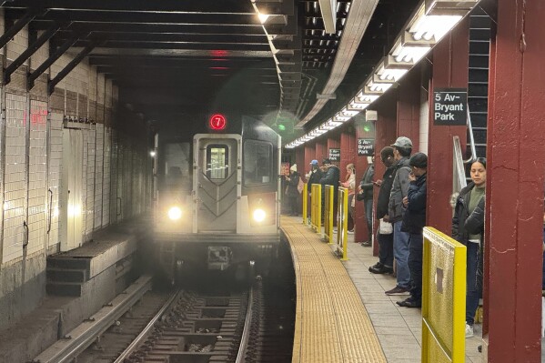 Subway riders stand near yellow barriers on a platform of the 7 train in New York on Tuesday, March 26, 2024. The city is experimenting with barriers to improve safety. (AP Photo/Cedar Attanasio)