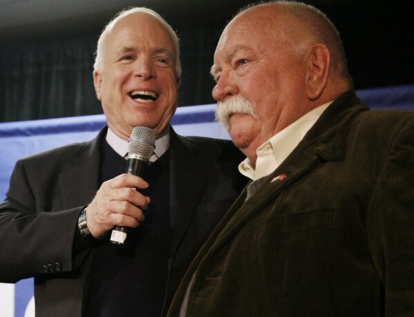FILE - In this Jan. 4, 2008, file photo, Republican presidential hopeful, Sen. John McCain, R-Ariz., left, introduces actor, Wilford Brimley, after making a reference to fellow Republican presidential hopeful, former Arkansas Gov. Mike Huckabee, campaigning with actor Chuck Norris, as McCain makes a campaign stop at Hudson Veterans of Foreign Wars Post 5791, in Hudson, N.H. Brimley, who worked his way up from stunt performer to star of film such as “Cocoon” and “The Natural,” has died. He was 85. Brimley’s manager Lynda Bensky said the actor died Saturday morning, Aug. 1, 2020 in a Utah hospital. (AP Photo/Charles Dharapak, File)