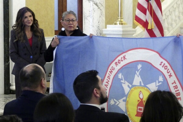 South Dakota Republican Gov. Kristi Noem, left, and Standing Rock Sioux Tribal Chairwoman Janet Alkire stand during a ceremony in which tribal leaders presented flags of the Standing Rock and Rosebud Sioux tribes, Wednesday, Jan. 10, 2024, at the state Capitol in Pierre, S.D. Alkire is holding the Standing Rock flag. (AP Photo/Jack Dura)